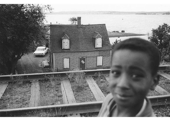 ZP_Young boy with, in the background, Ralph Jones' house boarded up for demolition_Africville, Halifax, Nova Scotia, Canada_1965_photo by Bob Brooks